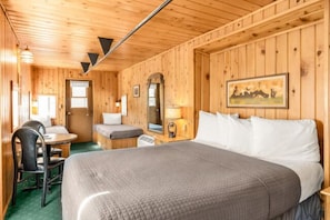 A wooden-paneled room with a bed, a desk, a chair, and a painting on the wall. - Jubilee Railroad Wilderness Lodge (Dunsmuir)