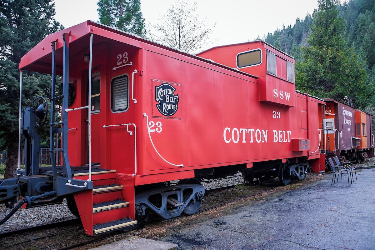 Ein roter Zugwagen mit der Aufschrift 'Cotton Belt Route' und 'SSW', geparkt auf Gleisen, Bäume im Hintergrund.