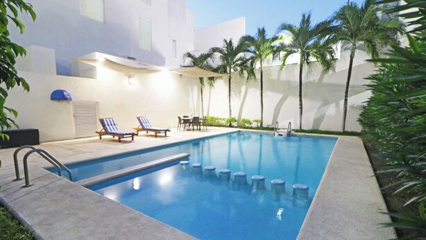 A swimming pool with blue tiles, surrounded by palm trees and lounge chairs. - Hotel Viajero Plus (Ciudad del Carmen)