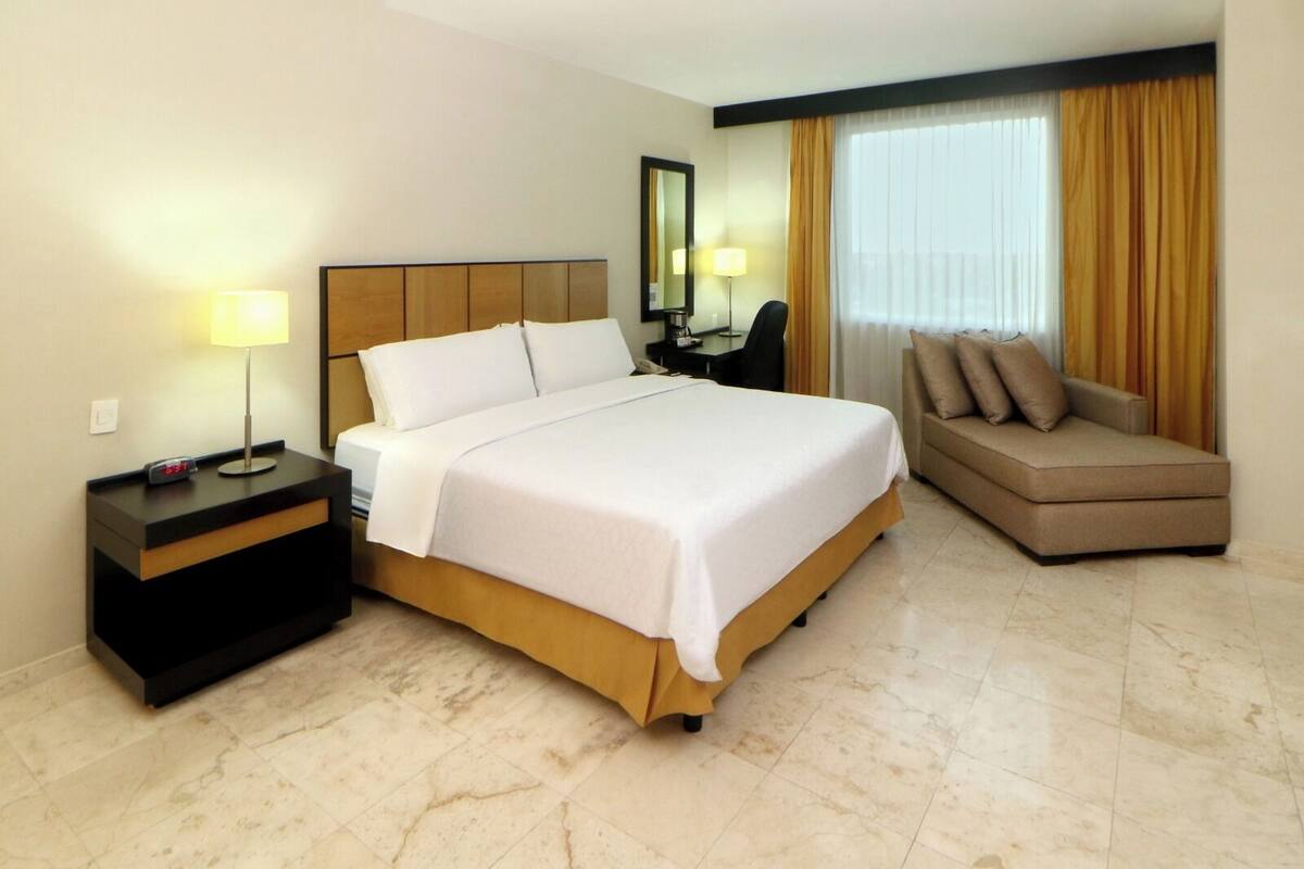 A hotel room with a bed, a desk, a chair, and a sofa.