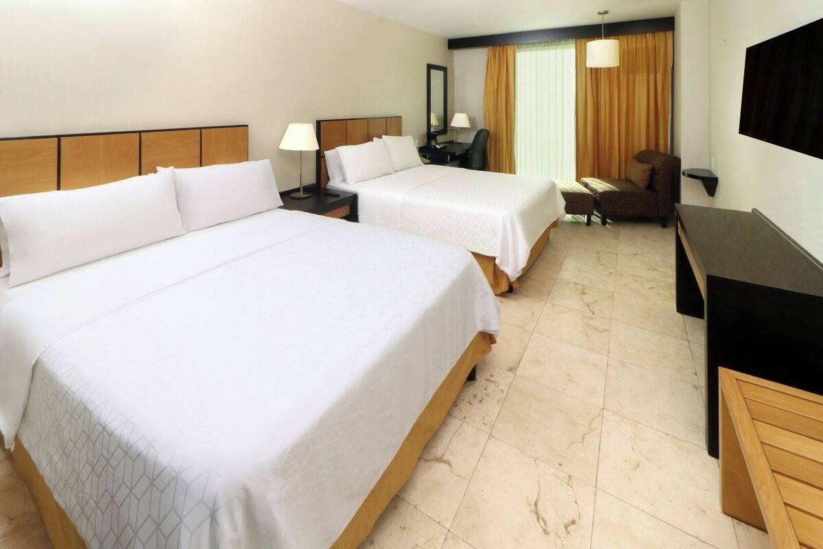 A hotel room with two beds, a desk, a chair, a TV, and a window with curtains.