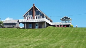 Uma casa grande de dois andares com varanda em volta, um pequeno edifício separado com varanda e um gramado bem cuidado.