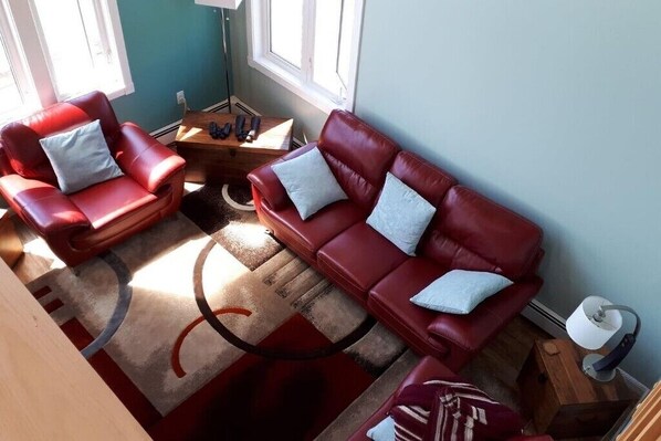 A living room with two red leather sofas, a coffee table, and a lamp. - Oceanfront PEI Home with Ocean Views, Wraparound Deck & Private Beach (Coleman)