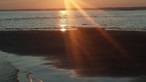 Um pôr do sol sobre uma praia, com águas calmas refletindo o sol.