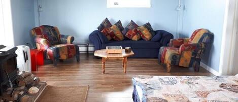 A living room with a blue sofa, colorful armchairs, a wooden coffee table, and a patterned rug.