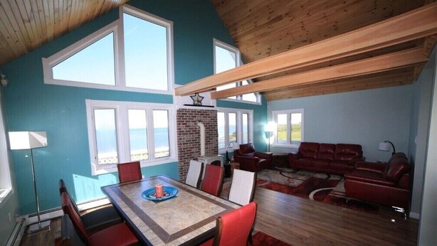 Uma sala de estar ampla, com um sofá vermelho grande, uma área de jantar com mesa e cadeiras, e uma lareira de tijolos.