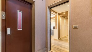 Entrada de hotel con puerta de madera, felpudo y pasillo que conduce a la recepción.