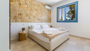 Una camera da letto con parete in pietra, un letto con lenzuola bianche, una finestra con stipiti blu e un piccolo cesto in vimini.