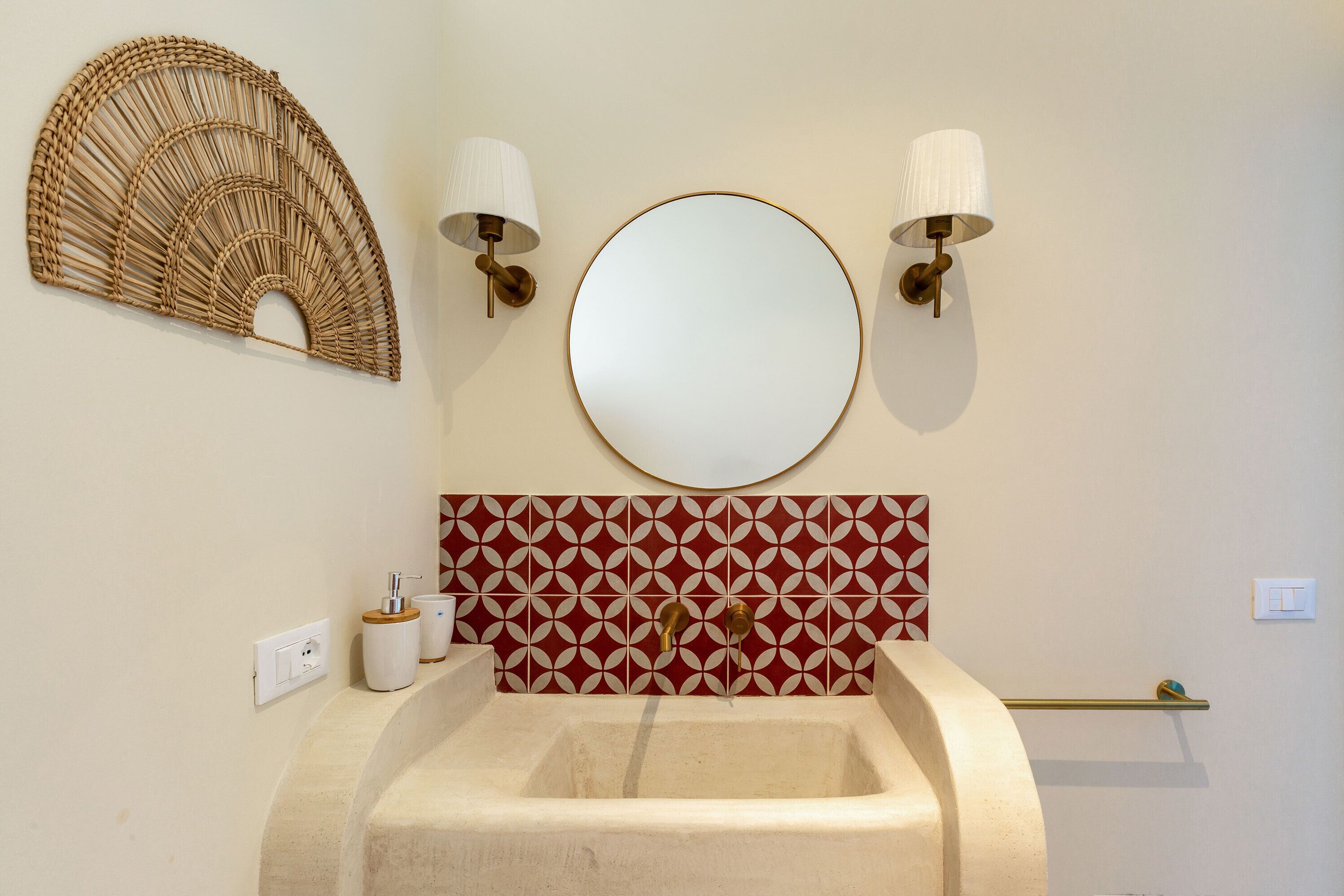A bathroom with a sink, two wall-mounted lights, a round mirror, and a decorative wall panel.
