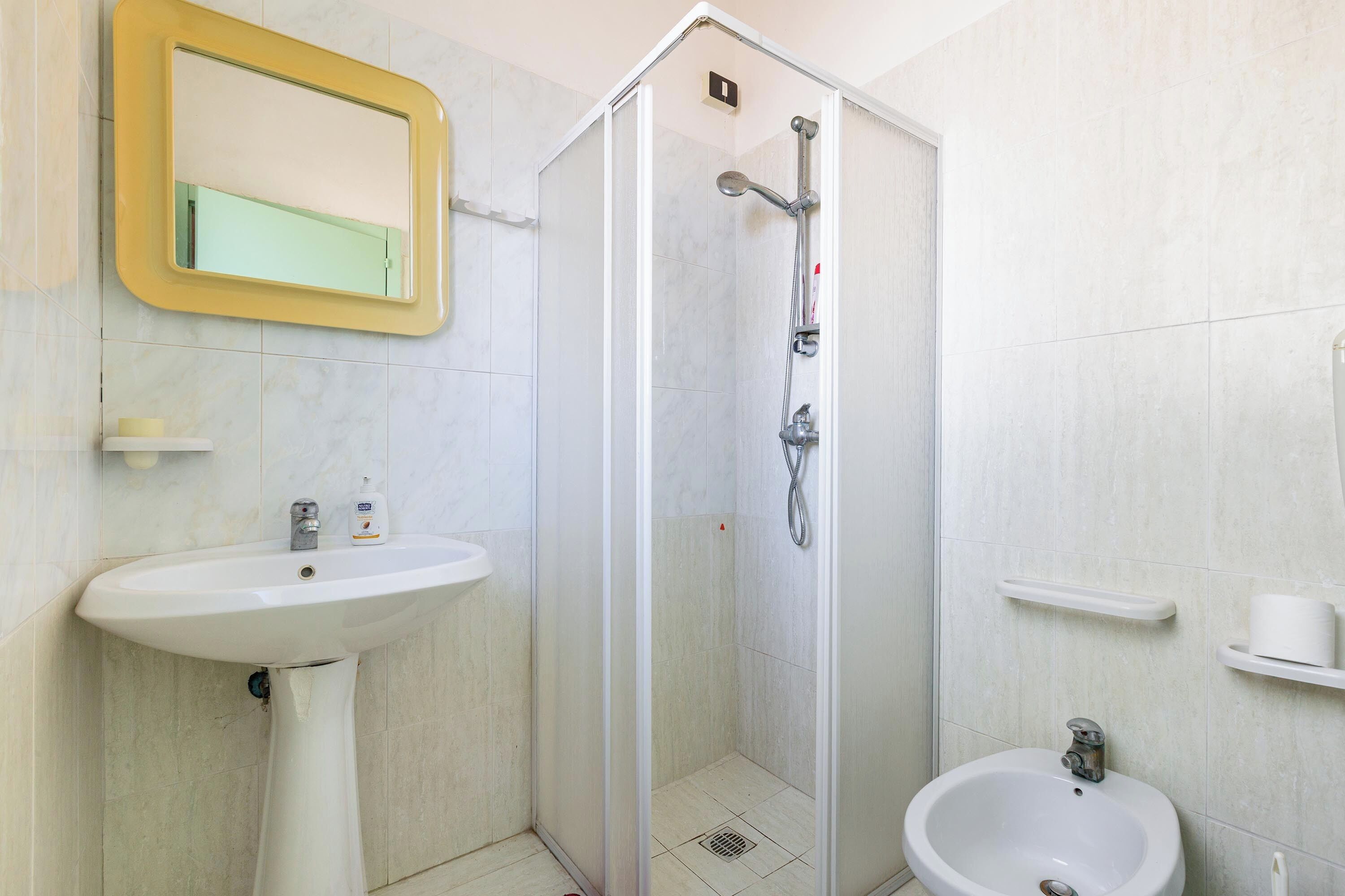 A bathroom with a white sink, a glass-enclosed shower, and a mirror with a yellow frame.