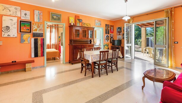 Uma sala ampla com uma mesa de jantar e cadeiras, um armário de madeira e uma poltrona vermelha.