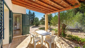 Um pátio externo com pérgola de madeira, uma mesa com cadeiras e vista para um jardim e árvores.