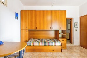 Ein kleines Zimmer mit einem hölzernen Bett, einem kleinen Tisch und einer Küchenzeile.