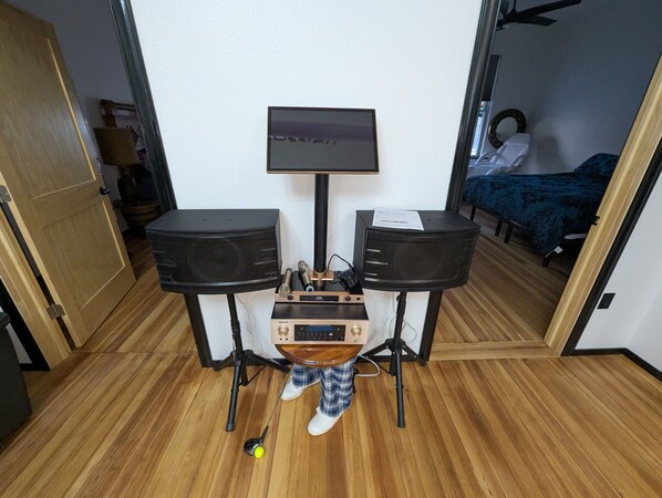 A compact room with a wooden floor, a bed with a blue blanket, and a desk with two speakers and a monitor. - Unique upstairs Escape in Lawrence with space, comfort, wine, golf, and dining. (Lawrence)
