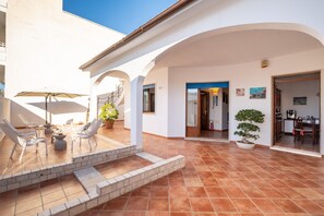 Un amplio patio exterior con zona de comedor, una escalera que sube a un nivel superior y una planta en maceta.