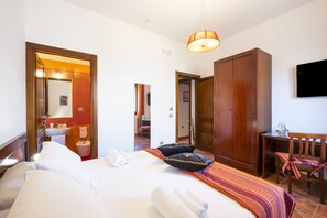 Habitación de hotel con cama, escritorio, silla, televisor y baño con espejo y lavamanos.
