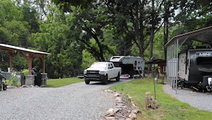 A gravel driveway leading to a covered area with a truck and a camper parked nearby. - Full 30 amp hookup on beautiful Deep Creek (Bryson City)