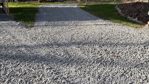 A gravel driveway leading to a wooden cabin with a covered porch and a shed in a rural setting. - Full 30 amp hookup on beautiful Deep Creek (Bryson City)