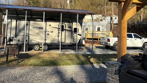 A recreational vehicle (RV) parked in a driveway with a covered outdoor area and a stone wall. - Full 30 amp hookup on beautiful Deep Creek (Bryson City)