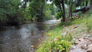 Ein Fluss mit klarem Wasser, umgeben von Felsen und viel Grün, mit einer Holzkonstruktion im Hintergrund.