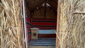 A rustic hut with a thatched roof, a colorful woven rug on the ground, and a simple wooden structure inside.