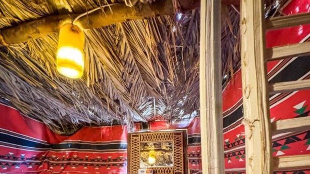 A room with a thatched roof, red and black striped walls, and a central wooden structure.
