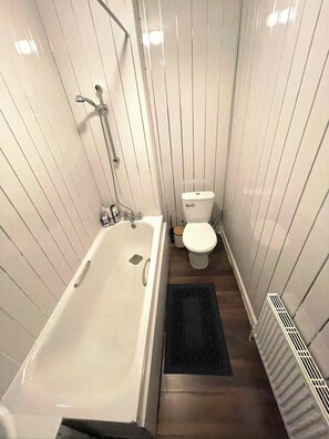 A small, narrow bathroom with a bathtub, toilet, and radiator. - Cosy Flat Near Kings Cross (London)