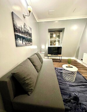 A modern living room with a sofa, a TV, a small side table, and a window with a view. - Cosy Flat Near Kings Cross (London)