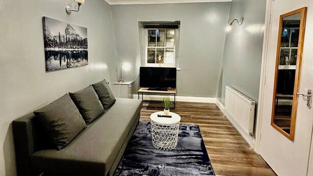 A living room with a grey sofa, a black rug, a white coffee table, and a painting on the wall. - Cosy Flat Near Kings Cross (London)