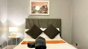 A neatly made bed with a headboard, a bedside table with a lamp, and a framed picture on the wall. - Cosy Flat Near Kings Cross (London)