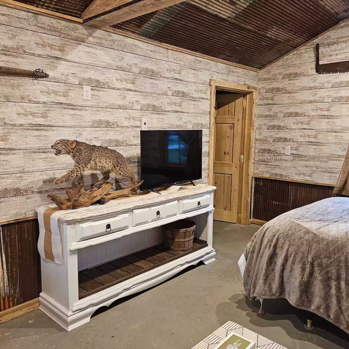 Ein rustikaler Raum mit einer Holzwand, einer weißen Kommode mit Fernseher darauf und einem Bett mit gemustertem Überwurf.