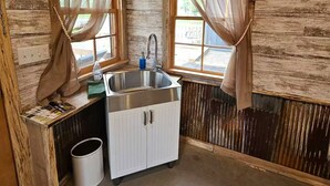 A rustic kitchen with wooden walls, a sink, and two windows with sheer curtains. - Relaxing Fun Bunk house 2 (Weyerhaeuser)