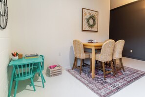 A dining area with a turquoise table and matching chairs, a patterned rug, and a framed artwork on the wall.