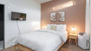 Een slaapkamer met een bed, bedlampen, een aan de muur bevestigde televisie en twee kunstwerken aan de muur.