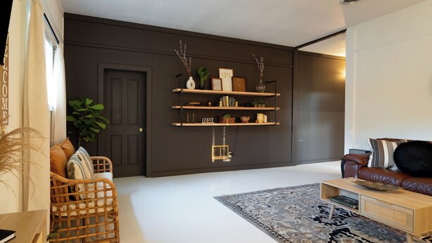 Een moderne woonkamer met een donkere muur, een rieten bank, een leren bank en een boekenkast met decoratieve objecten.