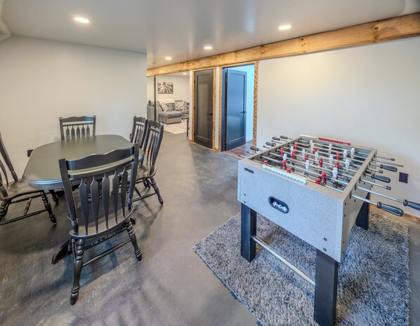 Une pièce avec une table de baby-foot, une table à manger avec des chaises et un canapé à l’arrière-plan.