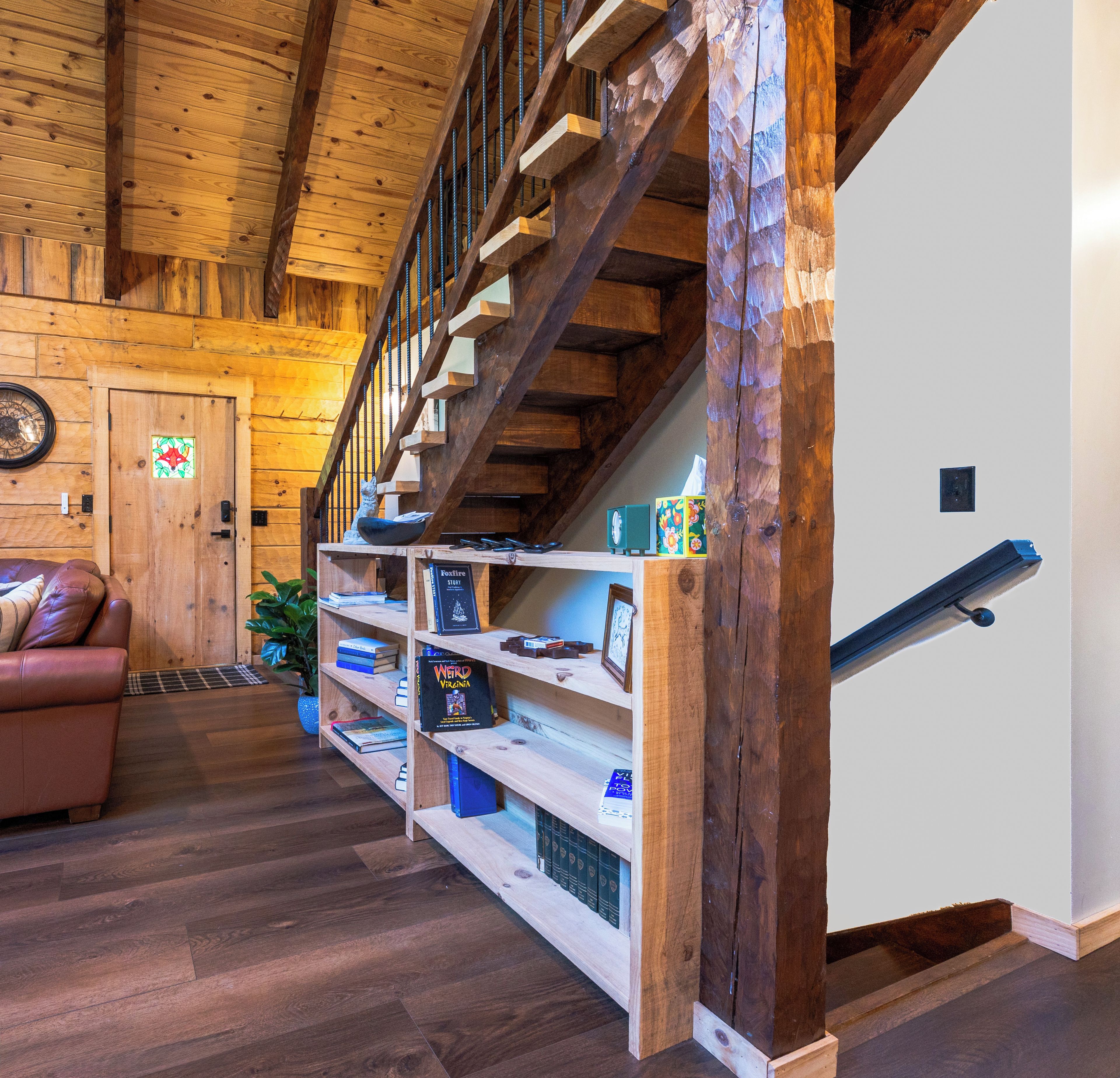 Una escalera de madera con barandilla, una estantería con libros y una puerta con un panel de vidrio decorativo.