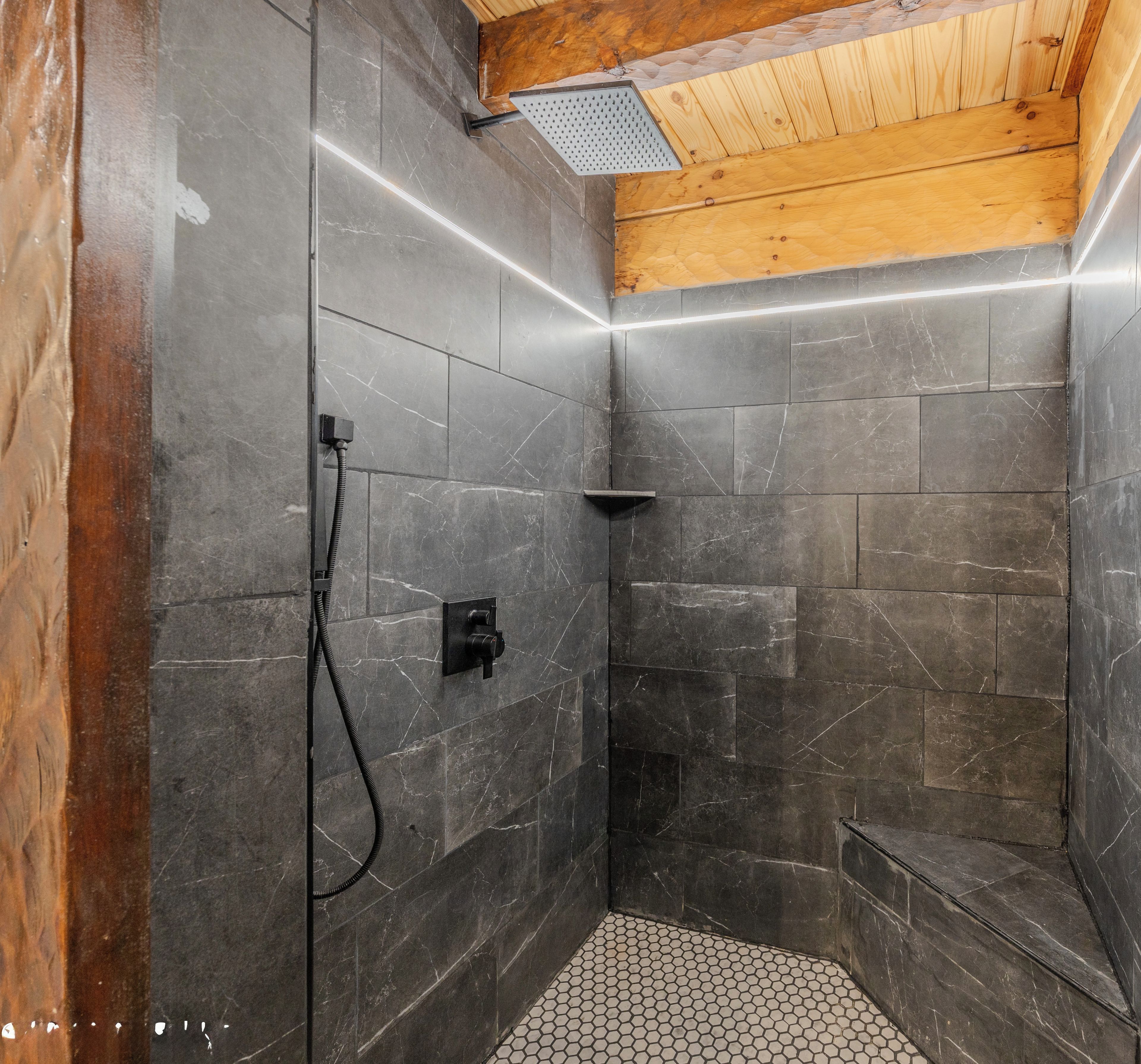 Un área de ducha con paredes de azulejos oscuros, techo de madera y piso de azulejos.