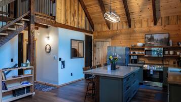 A spacious kitchen with wooden beams, a dining area with a large island, and a staircase leading to an upper level.