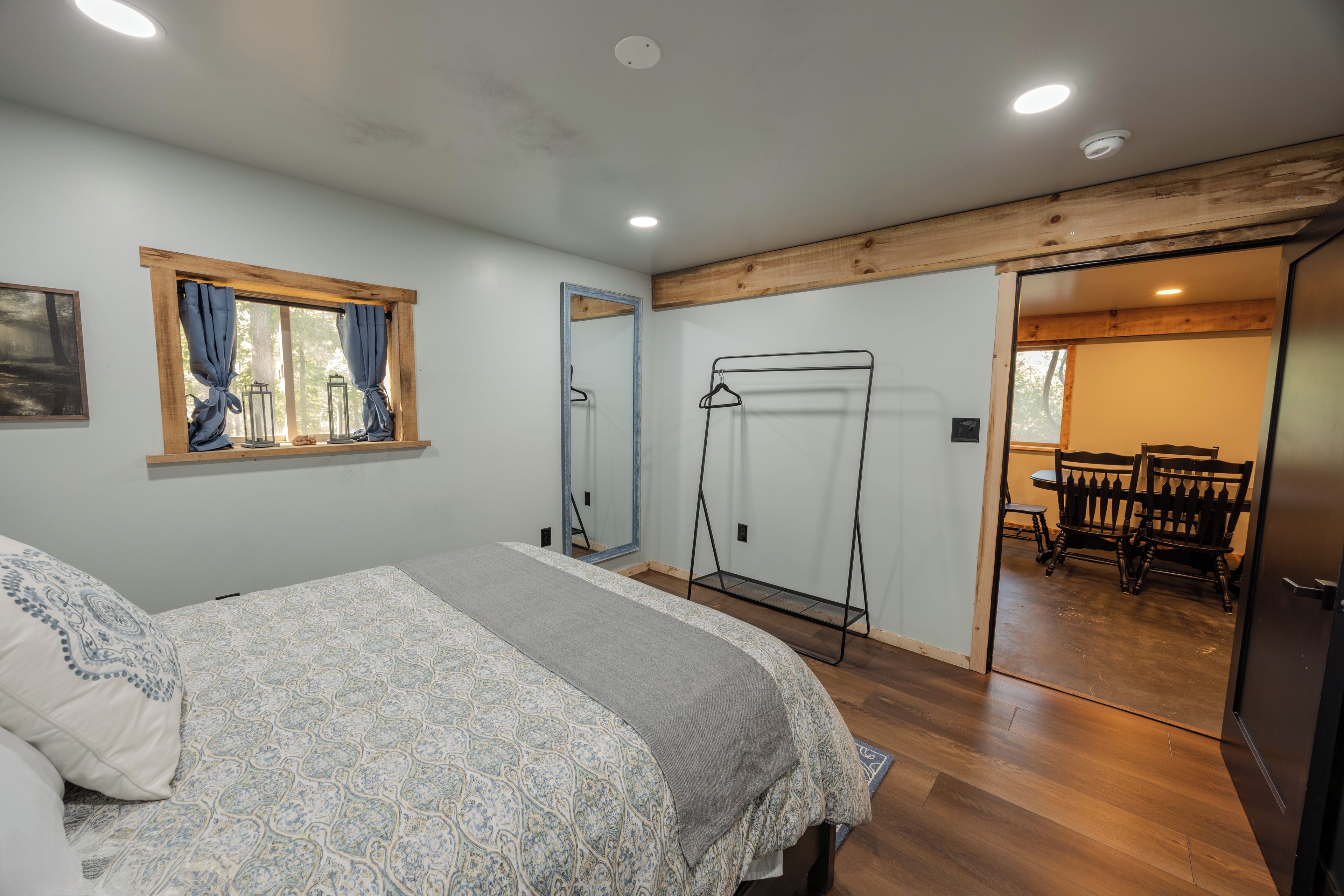 Un dormitorio con cama, ventana con cortinas, techo de madera y puerta que da a un comedor.