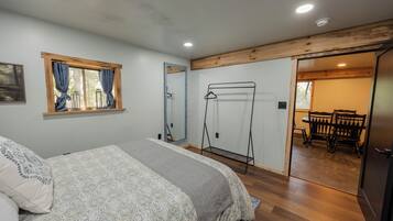 Un dormitorio con cama, ventana con cortinas, techo de madera y puerta que da a un comedor.