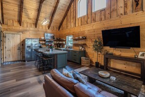 A cozy cabin interior with a wooden interior, a kitchen with a refrigerator, a dining area with a sofa, and a flat-screen TV mounted on the wall.