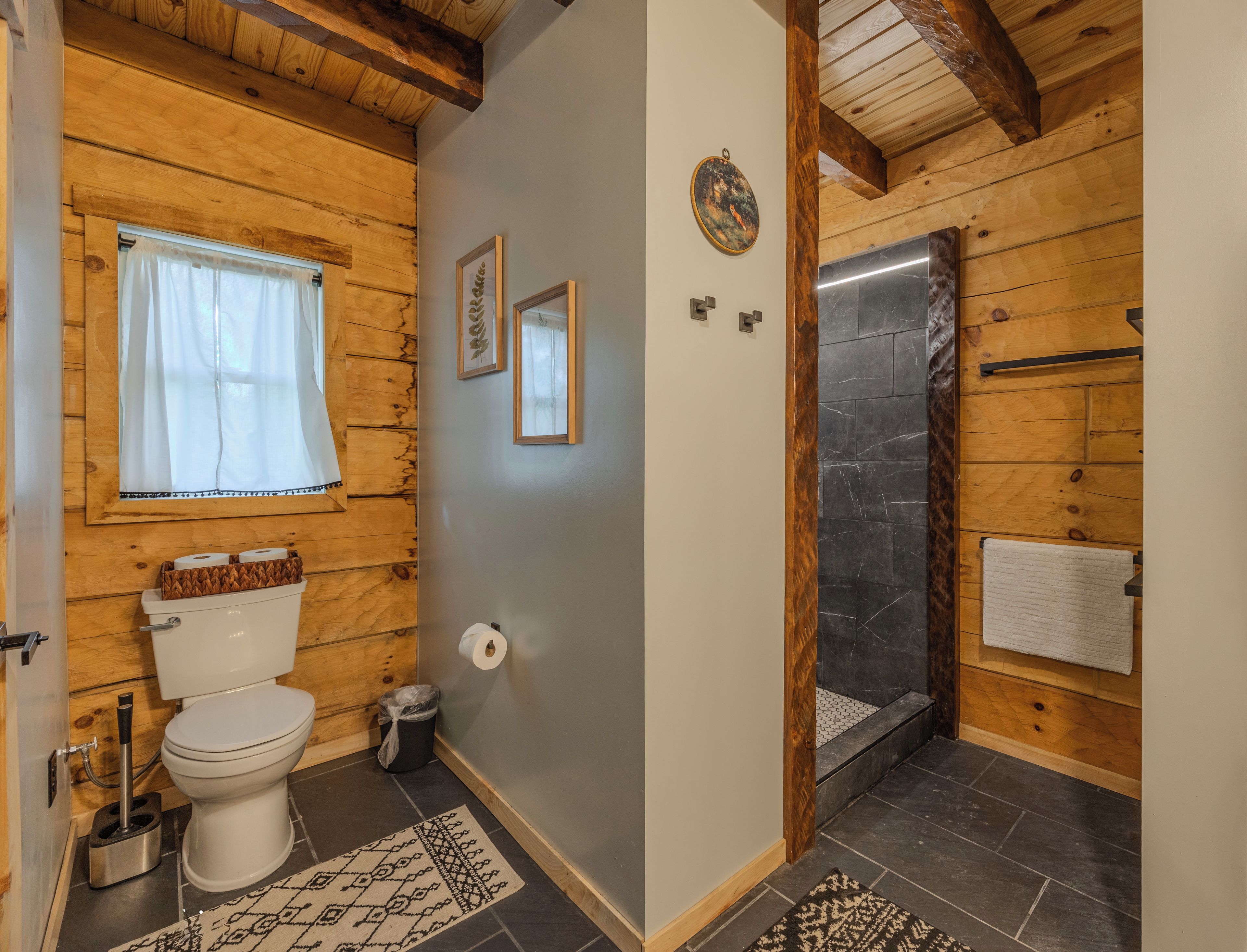 A wooden interior with a toilet, a shower, and a window with curtains.