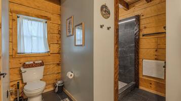 A wooden interior with a toilet, a shower, and a window with curtains.