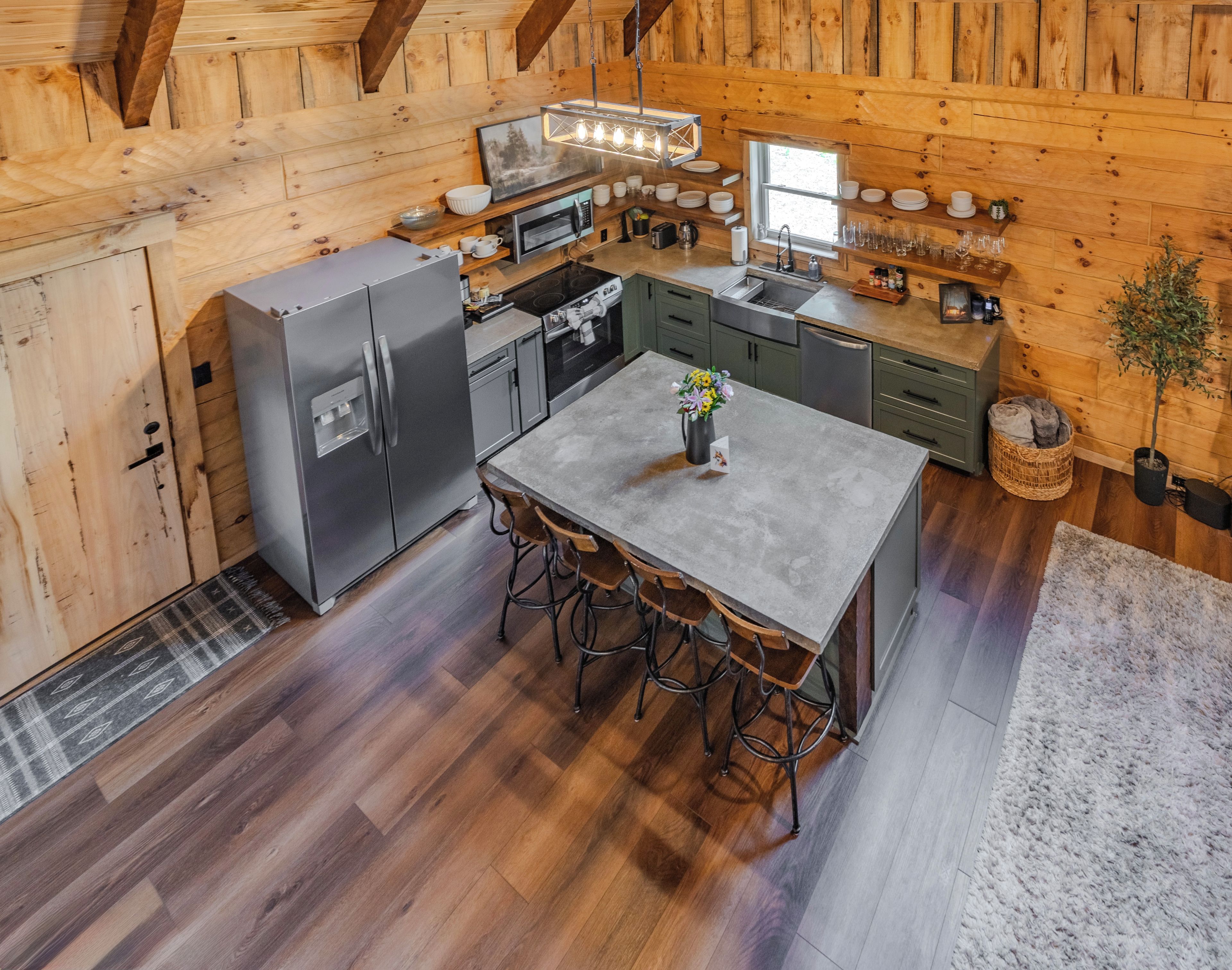 A compact kitchen with a refrigerator, stove, microwave, and sink. There is a dining table with chairs and a small potted plant.