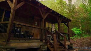 A wooden cabin with a porch and staircase, surrounded by trees.