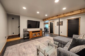 A modern living room with a flat-screen TV, a sofa, a glass coffee table, and a wooden entertainment unit.