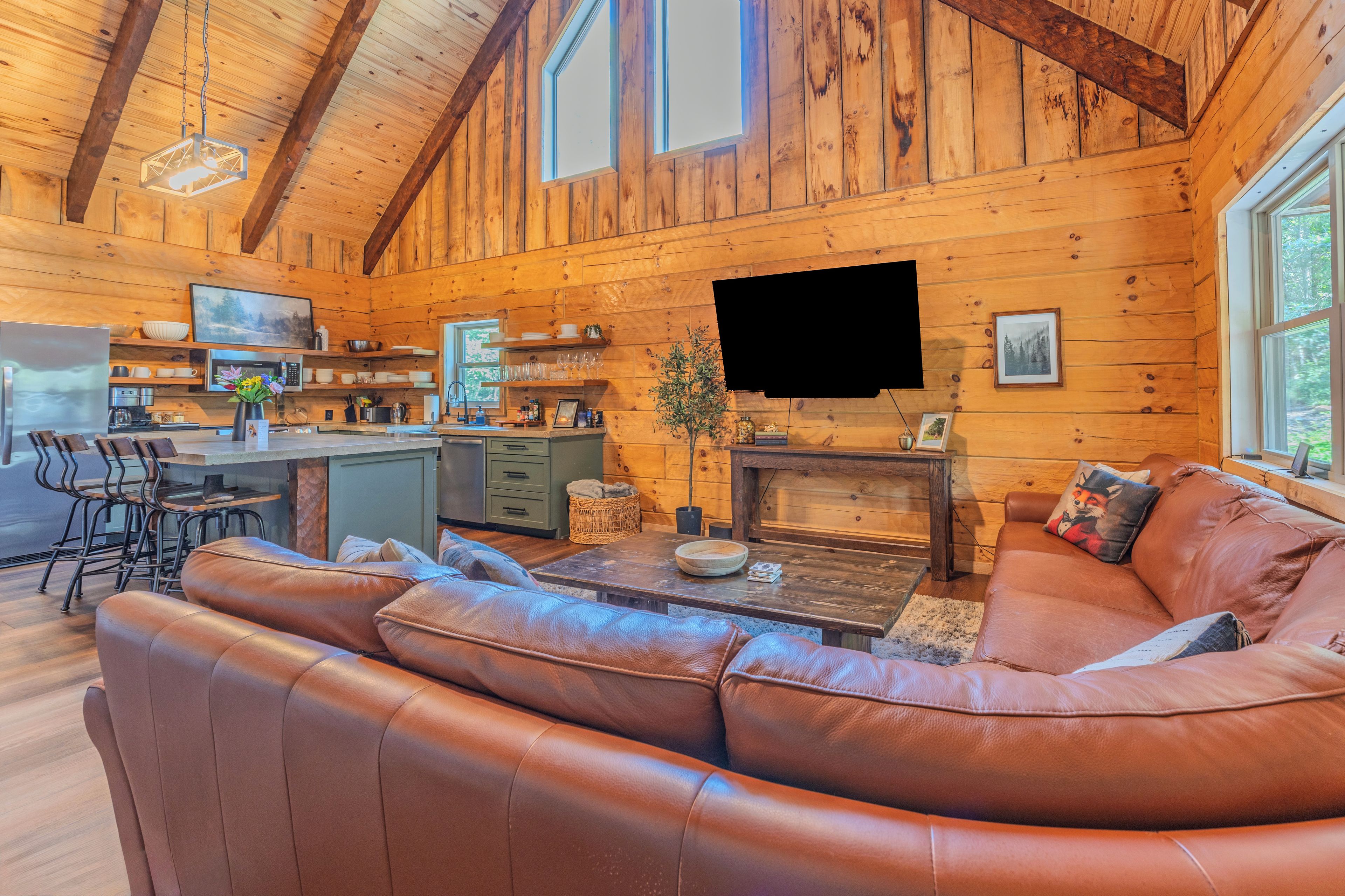 A cozy cabin interior with a wooden interior, a leather sofa, a dining area, and a kitchen.