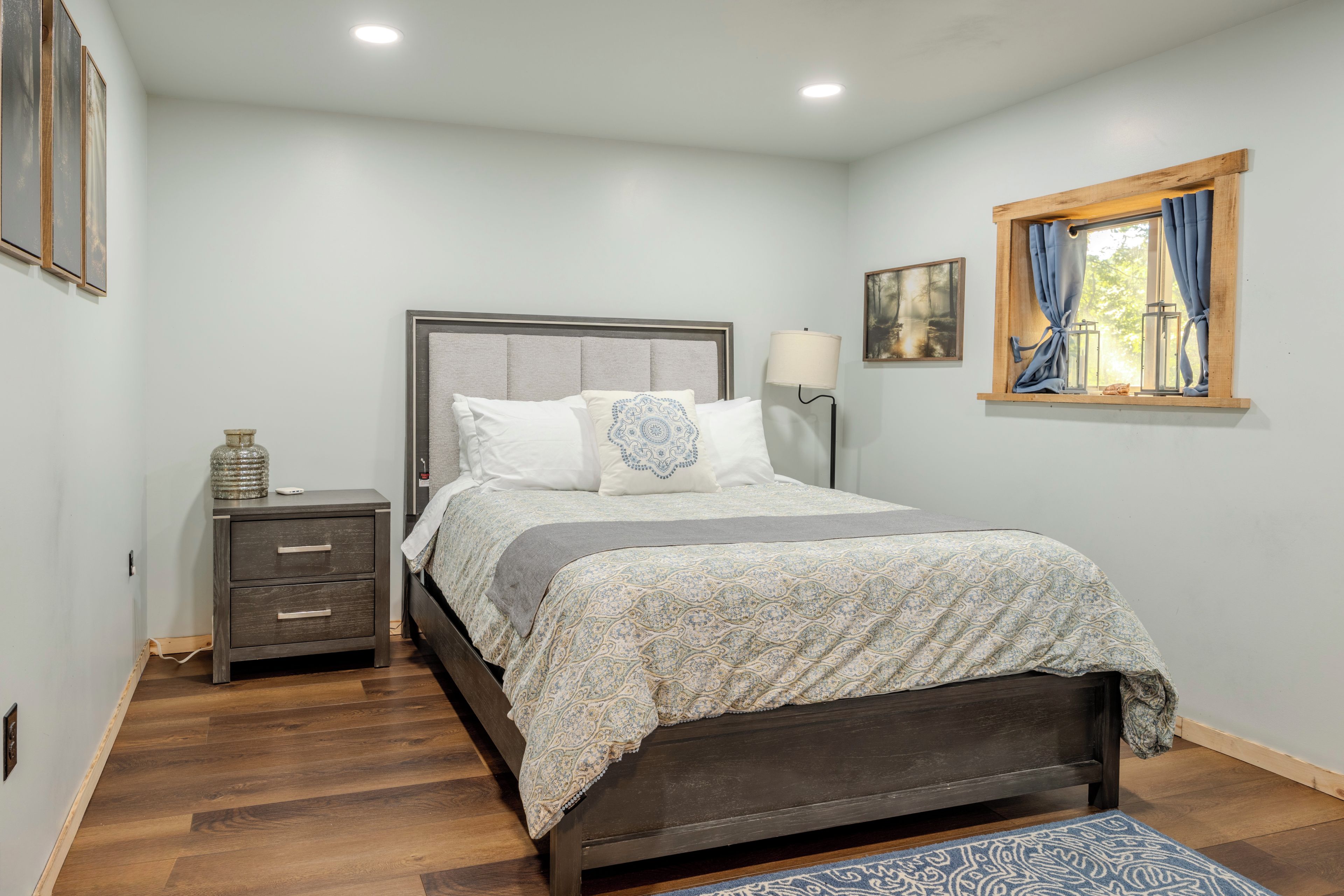 A bedroom with a bed, bedside table, lamp, and artwork on the wall.