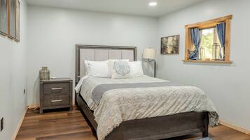 A bedroom with a bed, bedside table, lamp, and artwork on the wall.